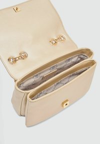 Beige læder håndtaske med en struktureret overflade, guldfarvede metaldele, to rum og et mønstret foer med cirkulære designs.