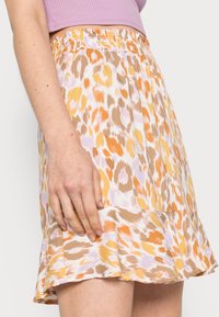 Saia curta e rodada em tecido leve, apresentando um padrão de estampado de leopardo nas tonalidades amarelo, laranja e bege, com uma cintura elástica.
