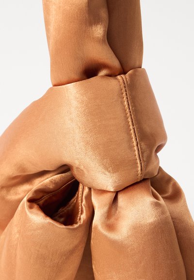 Sac en satin de couleur cuivre chaud et atténuée, présentant un design noué, une texture lisse et un éclat subtil avec des détails de couture visibles.