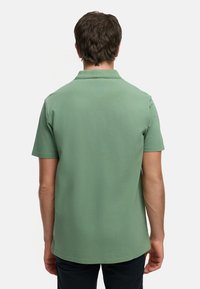 Grön kortärmad polo-skjorta, tillverkad av mjukt tyg, med krage och rak skärning. Har en slät yta utan mönster.