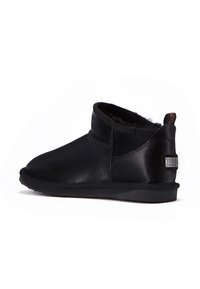 Botas de tobillo de cuero negro con un acabado suave, forro texturizado y suela plana. Presentan un parche con el logo de la marca en el talón.