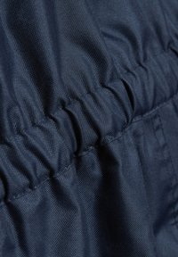 Mörkblått tyg med en texturerad yta, med elastiska rynkor och stygn, som visar veck och skrynklor i materialet.