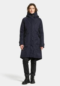 Marinblå långrock med huva, dragkedja fram, sidofickor och en något urfläkt nederdel. Bärs över svarta byxor och slitstarka snörstövlar.