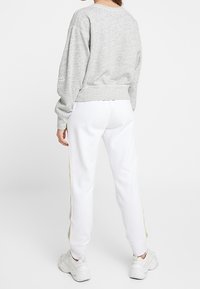 Sudadera gris claro de corte holgado con dobladillo acanalado. Combinada con pantalones de chándal blancos con detalles de franjas laterales. Zapatillas blancas completan el atuendo.