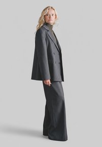 Szary dwurzędowy blezer z dopasowanymi spodniami o szerokich nogawkach, wykonany z gładkiej tkaniny o subtelnej fakturze, noszony na golfie.