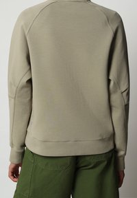 Sudadera beige con una textura suave, con mangas raglán y un dobladillo acanalado, combinada con pantalones cargo verdes.