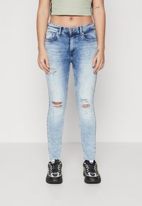 Lyseblå smale jeans med slitte detaljer, med høy midje og fire lommer. Kombinert med svarte og gule sportssko.