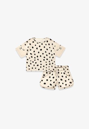 Ensemble beige composé d'une chemise à manches courtes et d'un short avec des taches noires irrégulières et des motifs de visage aux yeux fermés sur les manches et les poches du short.
