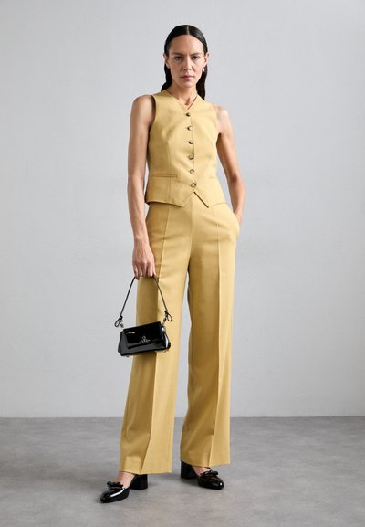 Gilet giallo su misura con bottoni e pantaloni a vita alta tapered, abbinati a una borsa e scarpe in pelle verniciata nera.