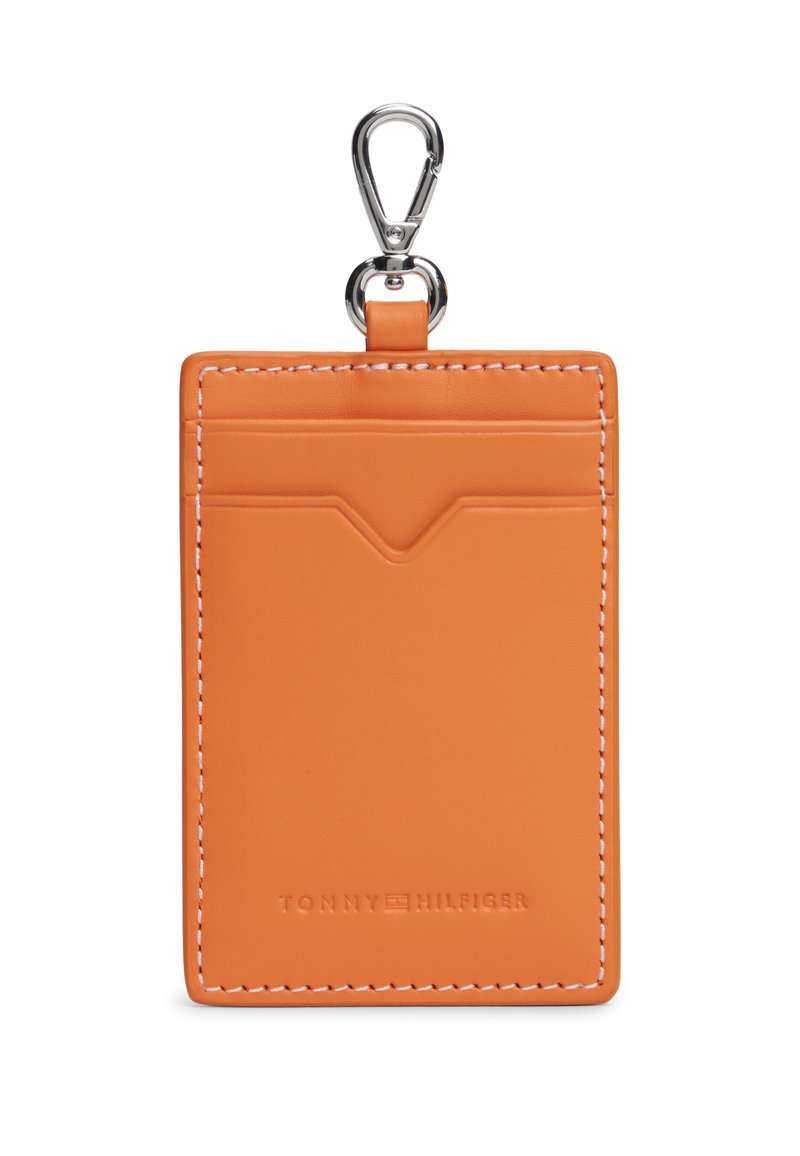 Πορτοκαλί δερμάτινη θήκη καρτών με λευκή ραφή, που διαθέτει πάνω τσέπη και ασημί κλιπ για προσάρτηση. Διακριτικό ανάγλυφο λογότυπο της μάρκας στο κάτω μέρος.