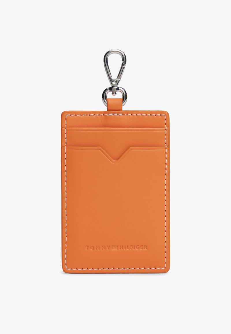 Πορτοκαλί δερμάτινη θήκη καρτών με λευκή ραφή, που διαθέτει πάνω τσέπη και ασημί κλιπ για προσάρτηση. Διακριτικό ανάγλυφο λογότυπο της μάρκας στο κάτω μέρος.