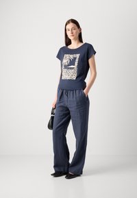 Navy cotton t-shirt with white graphic print, paired with loose-fit navy linen pants and black flats. Small black handbag, relaxed fit.