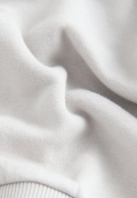 Valge puuvillane kangas siledapinnalise ja peene soonikmustriga. Materjal on pehmelt volditud, esitades õrna voldikust.