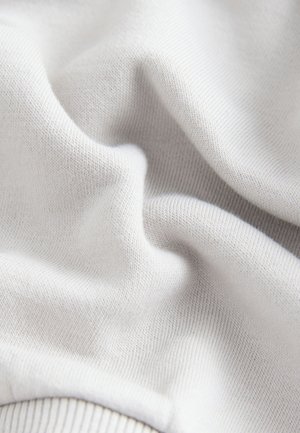 Witte katoenstof met een gladde textuur, voorzien van een fijn geribbeld patroon. Het materiaal valt soepel en toont zachte plooien.