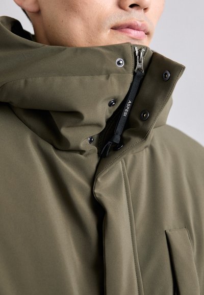 Giacca khaki con colletto alto, chiusura con zip e bottoni a pressione. Presenta una texture liscia e dettagli di cucitura rinforzata.