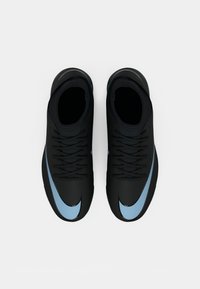 Las zapatillas deportivas negras presentan un logo de Nike en azul, material superior texturizado y cordones negros, con un silueta de perfil bajo y un diseño curvado.