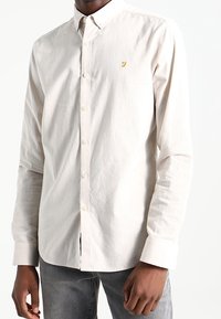 Hellbeige Hemd aus Baumwolle mit durchgehender Knopfleiste. Verfügt über einen strukturierten Kragen, lange Ärmel und ein dezentes gelbes Logo auf der Brust.