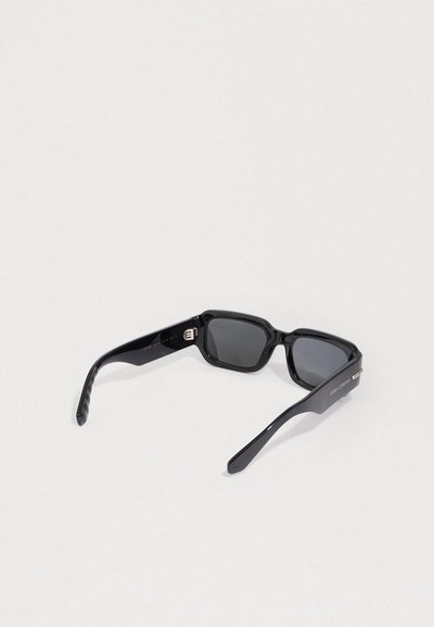 Fekete téglalap alakú napszemüveg sötét lencsékkel, vastag műanyag kerettel és egyenes szárakkal, amelyek belső oldalán finom csíkozás található.