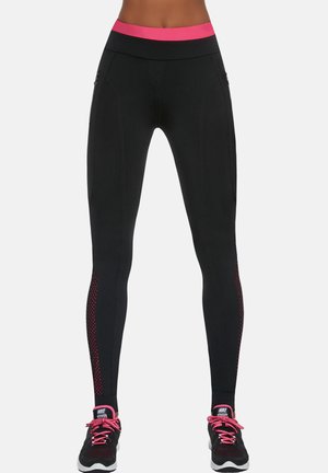 Kobiecy tors w czarnych legginsach z różowym pasem i dopasowanych czarno-różowych butach do biegania Nike, stojący na białym tle.