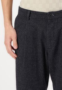 Pantaloni texturați de culoare gri închis, cu croială dreaptă, având închidere cu nasture și buzunare laterale. Materialul pare moale și uzat.