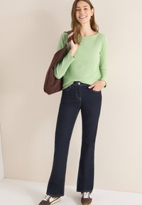 Zielony prążkowany top z długim rękawem, ciemne jeansy z rozszerzanymi nogawkami oraz brązowa torba na ramię. Trampki z białymi akcentami mają sznurowany design.