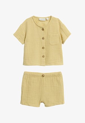 Keltainen puuvillainen taaperon setti, jossa on nappisuljettava lyhythihainen paita, jossa yksi rintatasku, ja siihen sopivat joustava vyötäröiset shortsit, joissa edessä nappi.