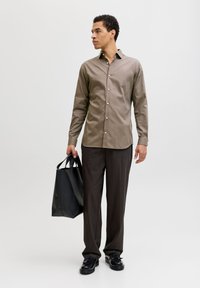 Μπλούζα με μακριά μανίκια σε μπεζ χρώμα με κουμπιά, συνδυασμένη με καφέ παντελόνια και μαύρα παπούτσια. Το άτομο κρατάει μια μαύρη τσάντα tote. Απλός, καθαρός σχεδιασμός.