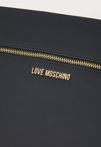 Sort tekstureret faux læderpung med en guldfarvet lynlås og præget "LOVE MOSCHINO" logo. Har en glat, mat overflade.