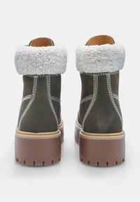 Stivaletti alla caviglia marroni e verde oliva con un soffice risvolto bianco, materiale scamosciato, suola in gomma spessa e dettagli di cucitura bianca a contrasto.