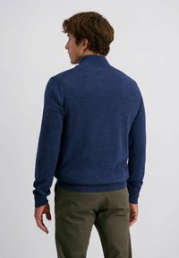 Dunkelblauer Strickpullover mit hohem Kragen, gerippten Bündchen und Saum, mit einer strukturierten Oberfläche und figurbetonter Silhouette. Über khakifarbene Hosen getragen.