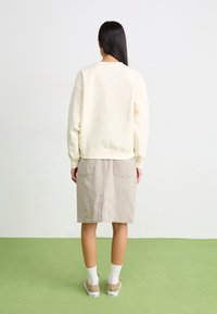 Cream sweatshirt with a relaxed fit, paired with a beige denim skirt. Long sleeves and ribbed cuffs, two back pockets on the skirt.