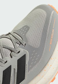 Vandtæt sportssko i lys grå med struktureret stofoverdel, sorte detaljer, grå snørebånd og en hvidspraglet sål.