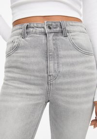 Jean gris taille haute en denim texturé avec un style classique à cinq poches et une finition légèrement délavée.