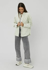 Chemise boutonnée vert clair avec un col structuré, coupe décontractée et tissu texturé, associée à un jean gris à jambes larges et des baskets blanches.