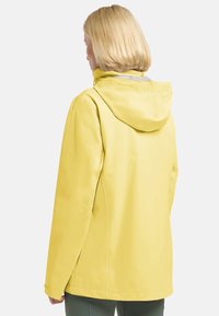 Gelbe wasserdichte Jacke mit Kapuze, glatte Textur und stromlinienförmiges Design. Verfügt über einen Rückenschlitz und minimale Hardwaredetails.