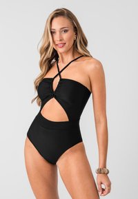 Maillot de bain noir une pièce avec un design découpé, un buste froncé et des bretelles croisées. Tissu lisse avec des jambes haute coupées et une texture solide.