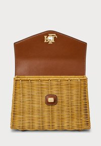 Υφασμένη τσάντα από άχυρο σε κίτρινο χρώμα με καφέ δερμάτινη επένδυση. Διαθέτει χρυσό κούμπωμα και ένα μικρό καφέ δερμάτινο στοιχείο στο μπροστινό μέρος.