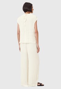 Crème-kleurig tweedelig outfit met een lichtgewicht, gekreukt textuur. Het topje heeft cap sleeves en een sleutelgat aan de achterkant; de broek is losjes passend.