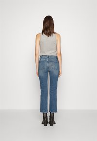 Šedý top bez rukávů a modré džíny s třepeným lemem. Černé kotníkové boty. Pohled zezadu ukazuje texturu látky a střih.