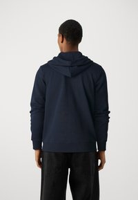 Felpa navy in morbido tessuto, con una vestibilità comoda, cappuccio con cordino e polsini a coste. Abbinata a jeans scuri.