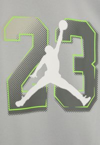 Tessuto grigio con un grande '23' in grigio scuro contornato di verde neon, e una silhouette bianca di una figura che salta con un pallone da basket.