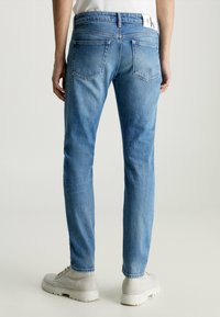 Vaqueros de mezclilla azul claro con un corte ajustado, que presentan una cintura de altura media, dos bolsillos traseros y detalles de costura mínimos. Llevados con zapatillas ligeras.