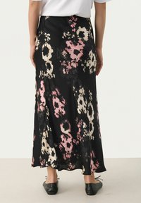 Jupe noire à fleurs avec des motifs abstraits roses et crème, fabriquée en tissu léger, avec une silhouette évasée et une coupe longue jusqu'aux chevilles.