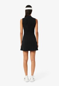 Vestito nero senza maniche con gonna plissettata, colletto e design della schiena aperta. Realizzato in un tessuto elasticizzato con dettaglio testurizzato sulla schiena.