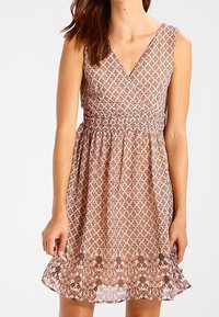 Brun mönstrad ärmlös klänning med V-ringning, insvängd midja och utsvängd fåll. Texturerat tyg med blomdetaljer längst ner.