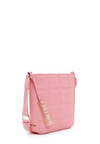 Różowa prostokątna torba na ramię z regulowanym paskiem, pikowanym wzorem w kratkę i metką z napisem "SURI FREY" przymocowaną do paska.