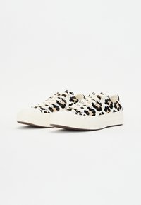 Zapatillas de lona con un estampado de leopardo en negro y beige, con suela blanca y puntera redonda, cordones planos y acentos laterales texturizados.