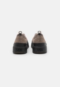 Brown suede sneakers featuring a black rubber sole, prominent back pull loops, and a rounded, chunky design for comfort and style.