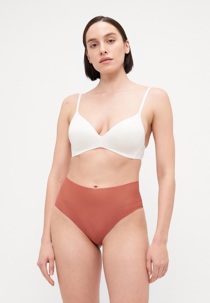 Bijela bežična bralette s dubokim izrezom, uparen s visokim gaćicama boje rđe, s glatkom teksturom i minimalističkim dizajnom.