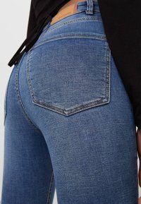 Vaqueros de mezclilla azul con un diseño ajustado, que cuentan con bolsillos traseros con detalles cosidos y una etiqueta de cuero en la cintura.